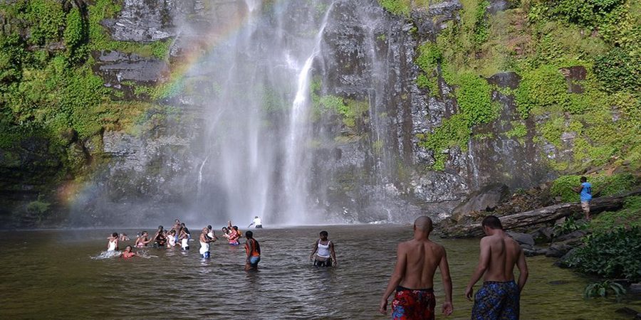 Visitors swimming beneath a rainbow at Wli Falls